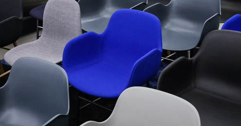 A collection of modern chairs, mostly gray and black, fills the space. One vibrant blue chair stands out.